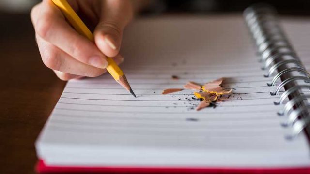 鉛筆でノートに書きこむ手のアップ